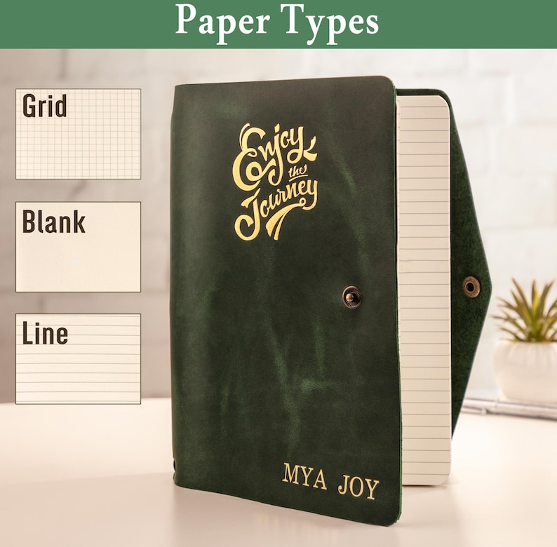 May include: A dark green leather journal with the words "Enjoy the Journey" in gold lettering. The journal is open, revealing lined paper. The text "MYA JOY" is printed at the bottom. The image also shows examples of grid, blank, and lined paper types.