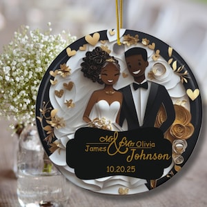 May include: Round wedding ornament featuring a smiling couple in formal attire. The ornament has a black border with gold accents, white paper cutouts, and gold hearts. The names "James & Olivia Johnson" and the date "10.20.25" are displayed on a black banner.