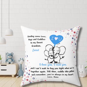 May include: White square pillow with a printed design. The design includes a blue heart-shaped balloon with "I U" inside, two hugging elephants, and text that reads "Sending some Love, Hugs and Cuddles to my Sweet Grandson, Lucas. I love you, I miss you...Love, Nana."