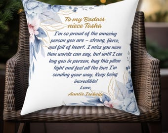 May include: A white throw pillow with a blue and gold floral design. The pillow has a message that reads "To my Badass niece Tasha I'm so proud of the amazing person you are - strong, fierce, and full of heart. I miss you more than words can say, but until I can hug you in person, hug this pillow tight and feel all the love I'm sending your way. Keep being incredible! Love, Auntie Isabelle"