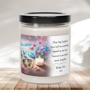 May include: A white candle jar with a label featuring a beach scene with footprints, butterflies, and flowers. The label also includes the text "Your tiny footprints have left an everlasting imprint on our lives. Forever in our hearts, never forgotten." and "Baby Ella 2024".