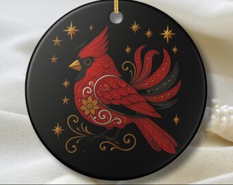 Può includere: Ornamento rotondo in ceramica nera con un design di cardinale rosso e dettagli dorati. L'uccello è posto su uno sfondo di stelle dorate ed elementi decorativi. Il testo in basso dice: QUESTO NON È UN ORNAMENTO 3D. L'IMMAGINE È STAMPATA SULLA PARTE ANTERIORE DI UNA SUPERFICIE IN CERAMICA BIANCA LISCIA.