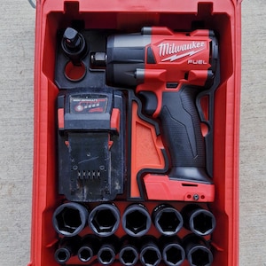 Puede incluir: Un kit de llave de impacto Milwaukee FUEL rojo en un estuche rojo. El kit incluye la llave de impacto, una batería y un juego de vasos. El estuche está abierto, revelando las herramientas cuidadosamente organizadas. El logotipo de Milwaukee es visible.