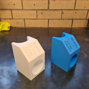 May include: Two 3D printed plastic pipe supports, one white and one blue. Both supports are labelled "3D-EDG" and have the dimensions "2.5" 90°" and "1.5D CLR".