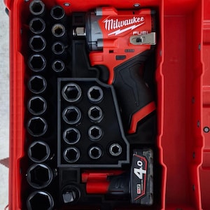 May include: A red Milwaukee FUEL impact wrench and accessories are stored in a red toolbox. The toolbox includes various black sockets and a 4.0 M12 battery. The Milwaukee logo is displayed on the impact wrench.