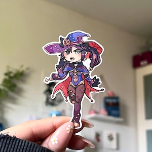 以下が含まれることがあります： 紫と青の髪をした女性キャラクターのカラフルな漫画のステッカー。赤と紫の帽子と青と金の衣装を着ています。キャラクターは杖を持っており、決意に満ちた表情をしています。