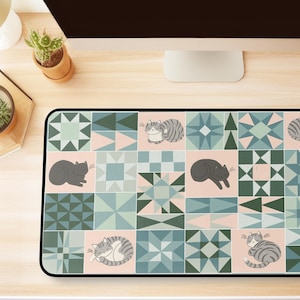 May include: A rectangular desk mat featuring a repeating grid pattern of geometric shapes in shades of sage green, dark forest green, and soft pink. The design includes various illustrations of sleeping cats in gray and white tones.