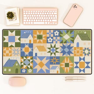 May include: A rectangular mouse pad with a patchwork design featuring houses, stars, and floral patterns in shades of blue, green, orange, and yellow. The pad is surrounded by a black border. A keyboard, phone, pens, and a mouse are on the white surface.