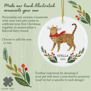 May include: A white ceramic ornament featuring a hand-drawn illustration of a tabby cat wearing a red scarf. The ornament is personalized with the name "STELLA" and the year "2024".