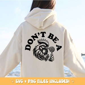 May include: Cream-colored hoodie with a black graphic on the back. The graphic features a detailed rooster holding a lollipop, with the words "DON'T BE A" above it. The hoodie is a casual style.