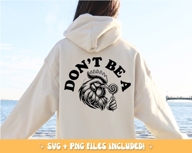 May include: Cream-colored hoodie with a black graphic on the back. The graphic features a detailed rooster holding a lollipop, with the words "DON'T BE A" above it. The hoodie is a casual style.