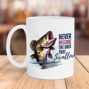 Op de afbeelding: Witte keramische koffiemok met een afbeelding van een baars die uit het water springt. De tekst op de mok luidt "Laat nooit degenen los die slikken."