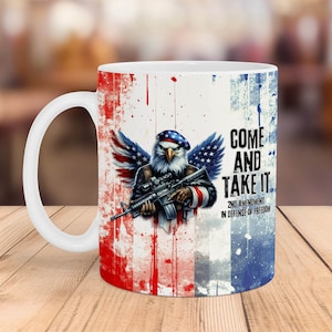 Pode incluir: Caneca de cerâmica branca com um design de bandeira americana vermelha, branca e azul. A caneca apresenta uma ilustração de uma águia careca segurando um rifle com o texto "Come and Take It" e "2nd Amendment in Defense of Freedom".
