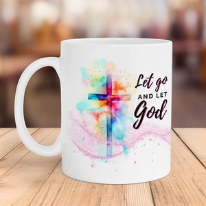 May include: White ceramic mug with a watercolor design of a cross in shades of pink, blue, yellow, and orange. The text "Let go and let God" is printed in black on the mug.