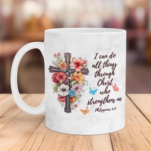 May include: White ceramic mug with a floral design and a cross. The mug has the text "I can do all things through Christ who strengthens me Philippians 4:13" printed on it.