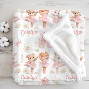 May include: A white baby blanket featuring a repeating pattern of dancing animal ballerinas in pink tutus. The blanket includes the name "Katelyn" and the date "12-12-2025" in pink script. Ballet shoes and floral accents complete the design.