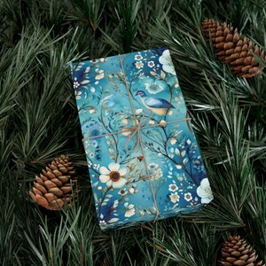 Pode incluir: Uma caixa de presente azul com um design floral e de p&aacute;ssaro. A caixa &eacute; embrulhada em papel azul com flores brancas e um p&aacute;ssaro azul com um galho marrom amarrado ao redor.