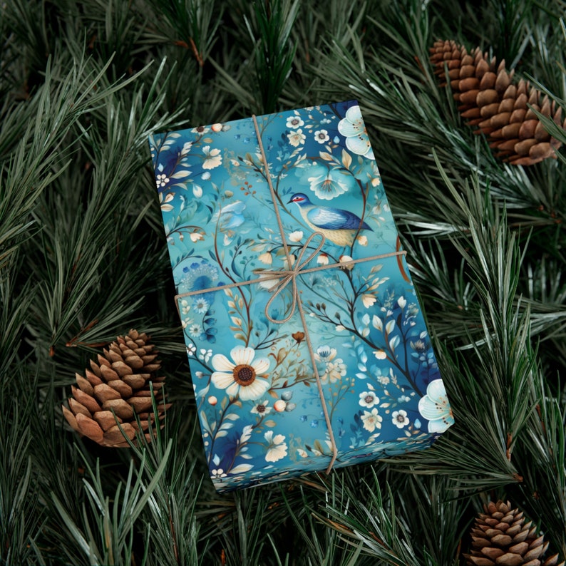 Pode incluir: Uma caixa de presente azul com um design floral e de p&aacute;ssaro. A caixa &eacute; embrulhada em papel azul com flores brancas e um p&aacute;ssaro azul com um galho marrom amarrado ao redor.