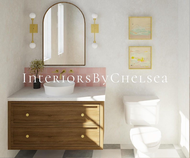 May include: A white bathroom with a wooden vanity with two drawers, a white porcelain sink, a white toilet, and a pink tile backsplash. The vanity has gold knobs. There is an arched mirror above the sink with two gold sconces on either side. There are two framed abstract paintings on the wall above the toilet.