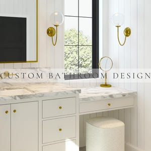 Puede incluir: Un mueble de baño con armarios blancos, pomos dorados y encimera de mármol. El espacio cuenta con un espejo con marco dorado, dos apliques de pared dorados con globos de cristal, un espejo de tocador dorado y un taburete texturizado.