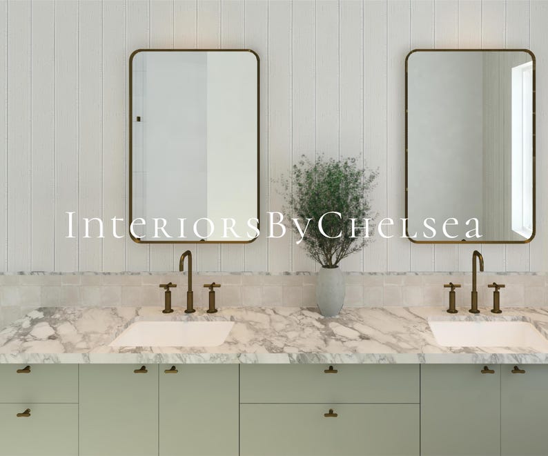 May include: A double vanity bathroom setup featuring two rectangular mirrors with thin bronze frames, white marble countertops, and sage green cabinets. Two bronze faucets are mounted above white sinks, with a vase of greenery in between.