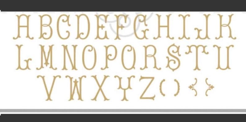 May include: A gold-colored alphabet with decorative flourishes. The letters are uppercase and include A through Z, as well as parentheses and two decorative symbols.