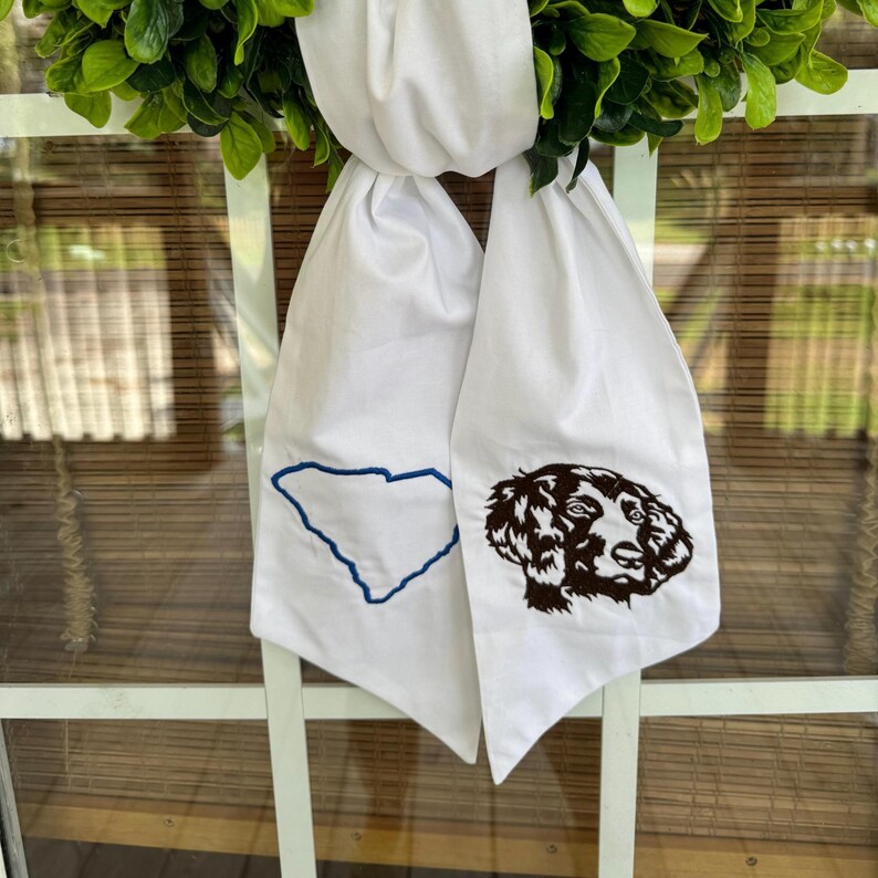May include: White fabric door swag with an embroidered outline of the state of South Carolina on one side and an embroidered brown dog head on the other side.