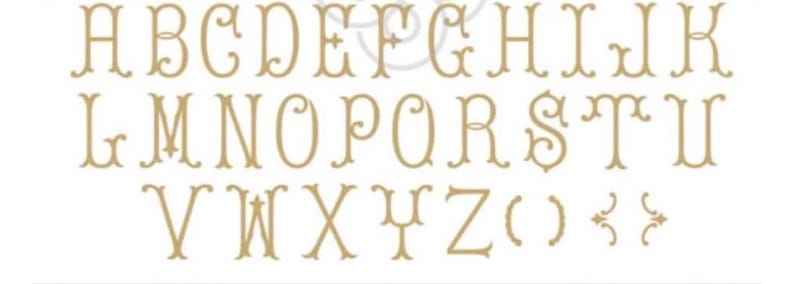 May include: A complete set of uppercase alphabet letters from A to Z in a light tan, decorative serif font with ornate flourishes. The characters are arranged in three rows, followed by a pair of parentheses and two small decorative bracket symbols.