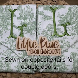 May include: Two white fabric panels featuring a green toile pattern and large embroidered green letters. A wooden sign reads Little Blue Heron Embroidery. Text on the image states: Sewn on opposite tails for double doors.