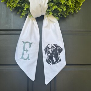 May include: White fabric door hanger with a black dog silhouette and the letter "E" embroidered in teal.