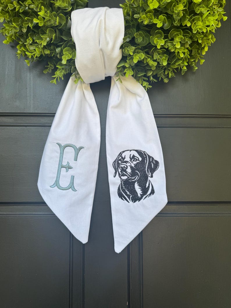May include: White fabric door hanger with a black dog silhouette and the letter "E" embroidered in teal.