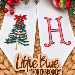 Peut inclure: Deux panneaux en tissu blanc avec broderie à la machine. Le panneau de gauche présente un sapin de Noël vert avec des ornements rouges et un nœud rouge. Le panneau de droite affiche une grande lettre H rouge rayée de blanc.