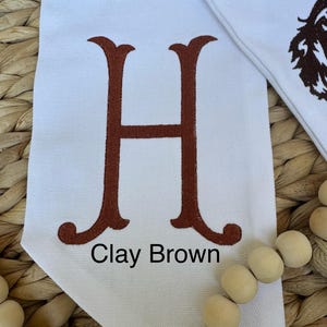 May include: White canvas banner with a large brown embroidered letter H and the text "Clay Brown" below it.