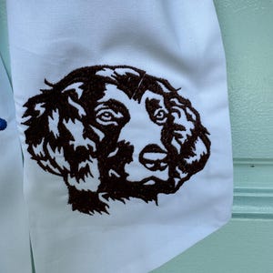 May include: Embroidered brown dog head on a white fabric background.