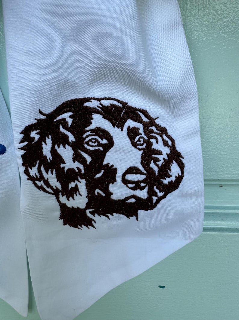 May include: Embroidered brown dog head on a white fabric background.