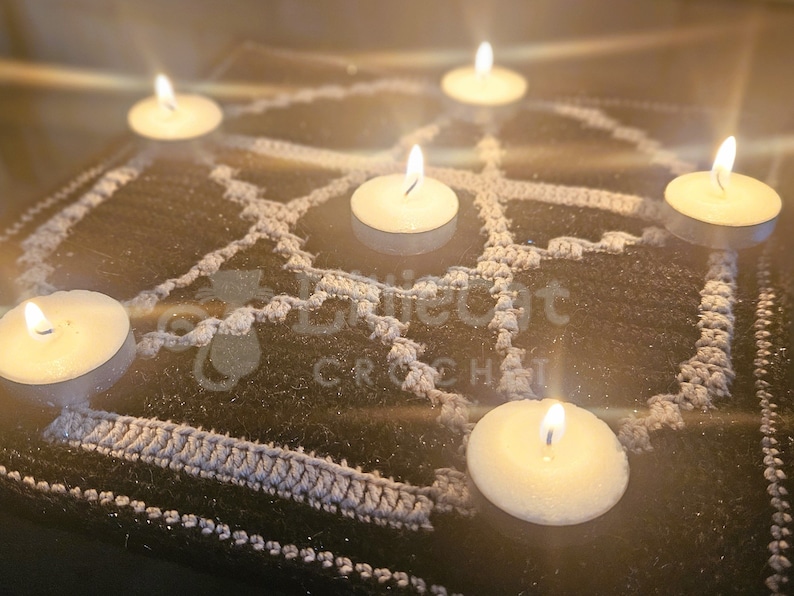 photo of an overlay mosaic crochet pattern. The pattern has a black background and a white motif of a pentagram on it. There are candles placed on each of the corners of the five pointed star and one in the middle. It has a wiccan atmosphere.