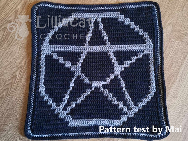 A crochet pattern using overlay mosaic crochet technique. The pattern has a dark background with a pale blue pentagram motif in the middle. The photo has an alternative and witchy feel. Text reads pattern test by Mai.