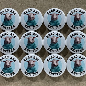 May include: Twelve white round buttons with a blue background and a sheep wearing a teal sweater. The buttons say "BAAD ASS KNITTER" in black text.