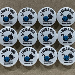 May include: Twelve white round buttons with black and blue cat illustrations. Each button says "I need a hug" and "Amount of yarn".