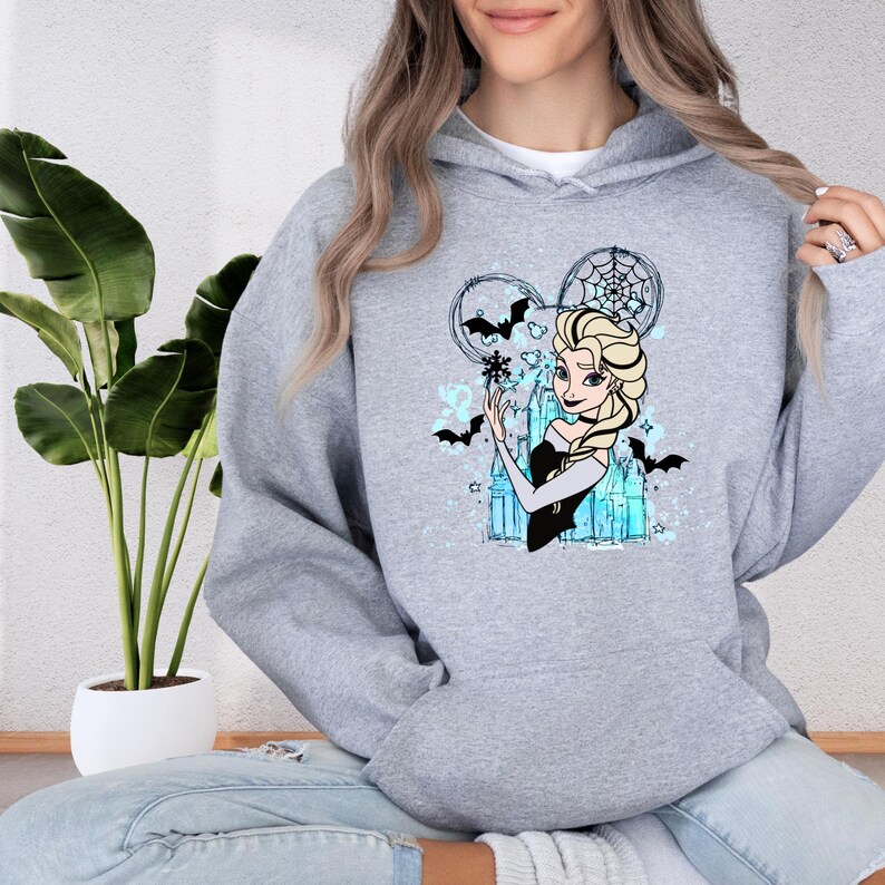 A woman wearing a grey hoodie with a graphic of a cartoon character, specifically Elsa from Frozen, is sitting on the floor next to a potted plant.