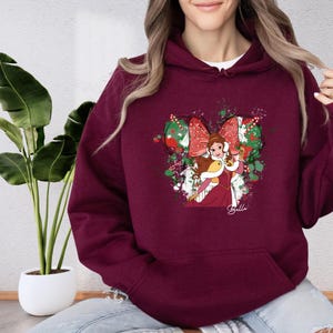 A woman wearing a burgundy hoodie with a graphic of a character from the Disney film Beauty and the Beast.