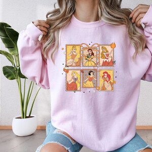 A woman wearing a pink sweatshirt with a graphic of Disney princesses.
