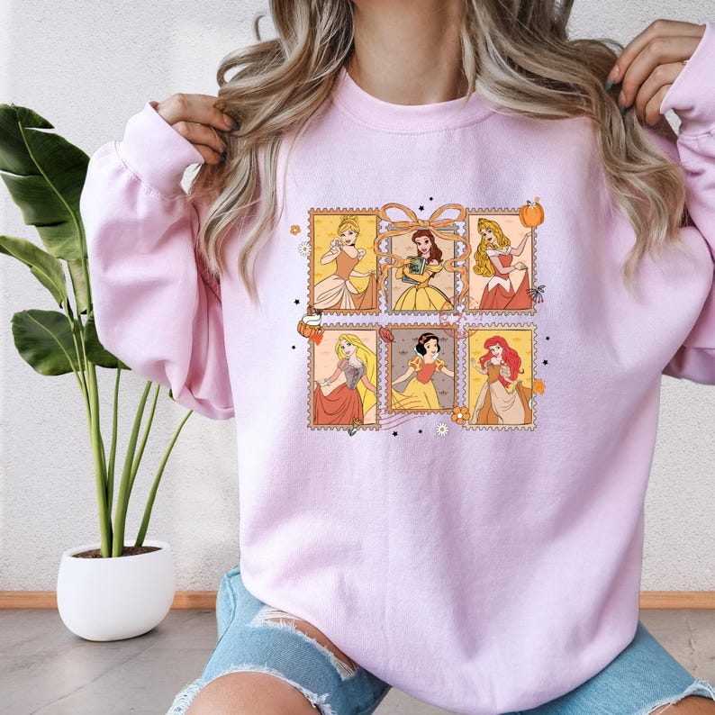 A woman wearing a pink sweatshirt with a graphic of Disney princesses.