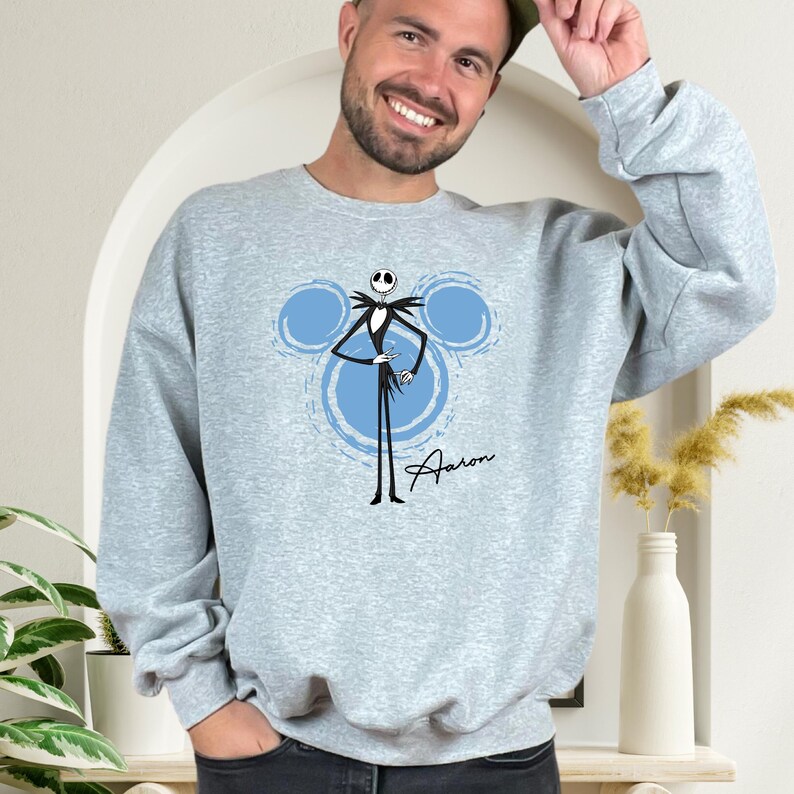 A man wearing a gray sweatshirt with a graphic of a skeleton and Mickey Mouse design, smiling and posing for the camera.