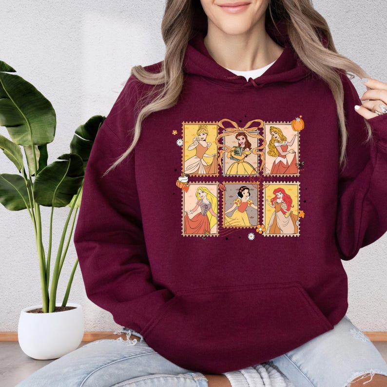 A woman wearing a burgundy hoodie with a graphic of Disney princesses on it.