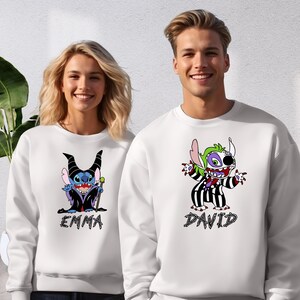 A man and a woman are standing next to each other, both wearing white sweatshirts with cartoon characters printed on them.