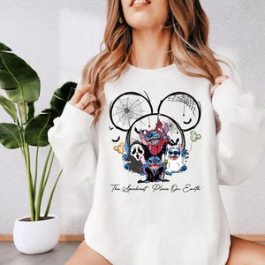 A woman wearing a white sweatshirt with a graphic design featuring a character from Disney's "The Darkest Place on Earth".