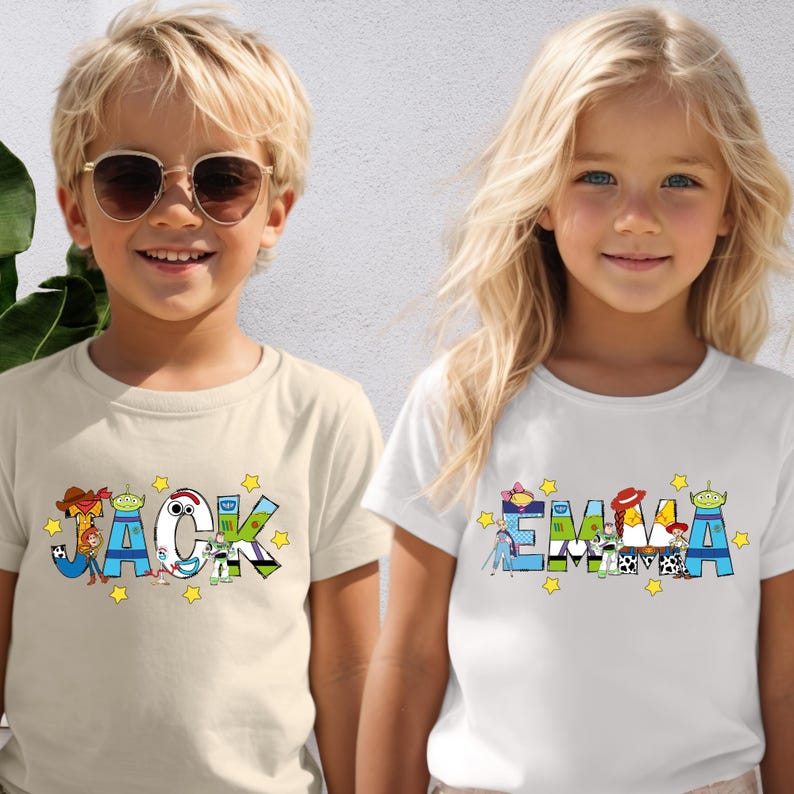 May include: Two children wearing t-shirts with personalized names. The shirt on the left says "JACK" with colourful cartoon character designs. The shirt on the right says "EMMA" with similar designs. Both shirts have yellow star accents.