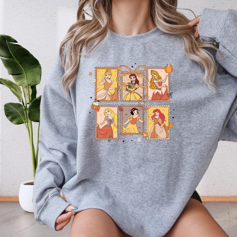 A woman wearing a gray sweatshirt with a graphic design featuring illustrations of Disney princesses.