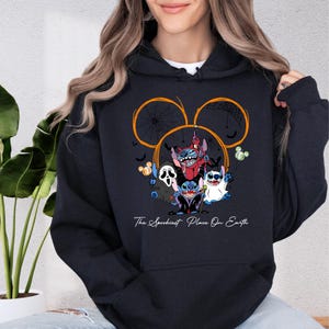 A woman wearing a black hoodie with a graphic design featuring characters from the Disney movie "Stitch".
